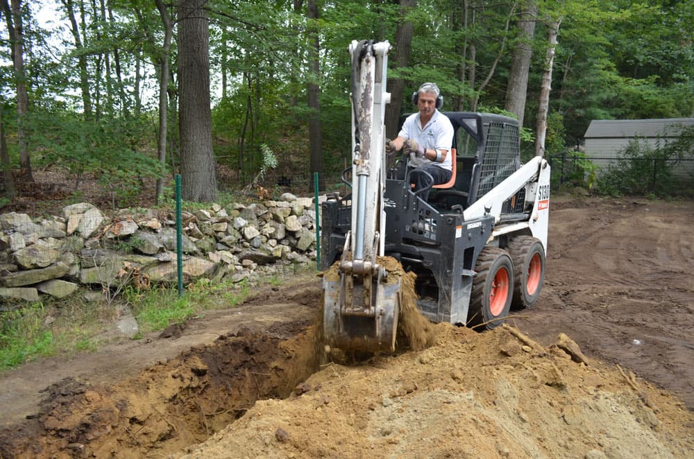 Bobcat compact loader fitted with a backhoe arm parked at a trenching jobsite