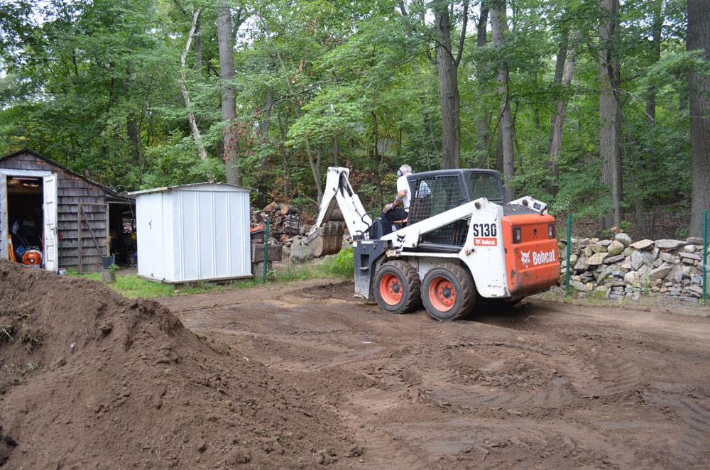 Drainage trench started across a lawn with soil laid to the side of the cut